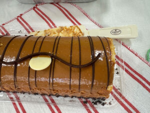 Porto's Bakery의 Dulce De Leche Cake Roll 케이크 롤 전체 샷. 진한 카라멜 색의 둘세 데 레체 코팅과 다크 초콜릿 장식이 된 모습.